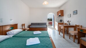 A hotel room with two beds, a sofa, a dining table with chairs, a wooden cabinet, and a view through an arched doorway. - Apartment 'Studio 6' with Sea View, Wi-Fi and Air Conditioning (Naxos Chora)