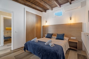 A bedroom with a wooden headboard, two bedside tables, a bed with blue bedding, and a bathroom visible through an open door.