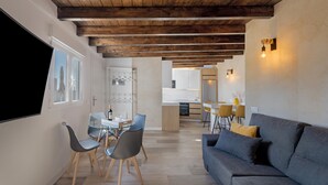 A modern living room with a grey sofa, wooden ceiling beams, a dining area with chairs and a table, and a kitchen in the background. - Holiday Home 'Miranda 2' with Sea View, Wi-Fi and Air Conditioning (Igueste de Candelaria)