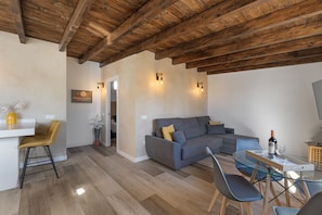 A modern living room with a wooden ceiling, a grey sofa, a glass dining table, and a yellow chair.