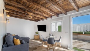 A modern interior with a wooden ceiling, a grey sofa, a dining table with chairs, and a TV mounted on the wall. - Holiday Home 'Miranda 2' with Sea View, Wi-Fi and Air Conditioning (Igueste de Candelaria)