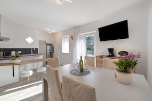 A modern kitchen with a dining area, a flat-screen TV, and a potted orchid on the table.