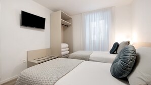 Ein Hotelzimmer mit zwei Betten, einem Fernseher, einem Schrank und einem Fenster mit Vorhängen.