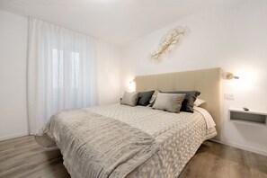 A bedroom with a large bed, a bedside table, a wall-mounted light, and a decorative wall piece.