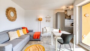 A modern living room with a grey sofa, a dining table, and a kitchen in the background. - Superb Apartment on Fishermen's Island with Sea View, Private Terrace & Air Conditioning (Agde)