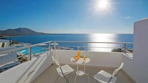 A balcony with a pool, white chairs, and a table with drinks.