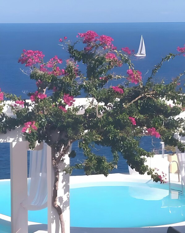 A poolside view with a clear blue sky, a sailboat on the water, and pink bougainvillea flowers. - Apartment 'Kaladi Rock' with Sea View, Shared Pool and Wi-Fi (Avlemonas)