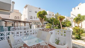 A terrace with a glass table and chairs, surrounded by a white decorative fence, with buildings and trees in the background. - Holiday Home 'Spacious' with Shared Pool, Wi-Fi, and Air Conditioning (El Campello)