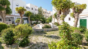 A courtyard with white buildings, trees, and a stone bench. - Holiday Home 'Spacious' with Shared Pool, Wi-Fi, and Air Conditioning (El Campello)