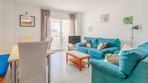 Ein Wohnzimmer mit einer Couch, einem Fernseher, einem Essbereich mit Stühlen und einem Balkon mit Blick.