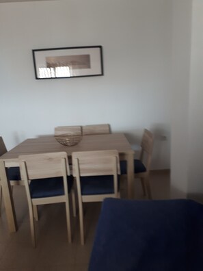 Ein Essbereich mit Holztisch und Stühlen, einem gerahmten Bild an der Wand und einem blauen Sofa im Vordergrund.