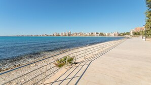 A coastal walkway with a clear view of the sea and a distant city skyline.