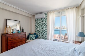 Ein Hotelzimmer mit Bett, Schminktisch, Spiegel, Fenster mit Blick auf die Stadt und Balkon mit Sitzgelegenheiten.