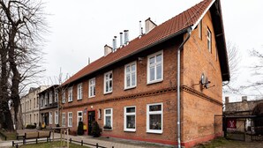 Un bâtiment en briques avec un toit recouvert de tuiles rouges, de nombreuses fenêtres et une entrée fermée par un portail.