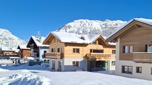 Un resort invernal cubierto de nieve con edificios de madera, un telesilla y un cielo azul despejado.