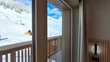 A room with a large window overlooking a snowy mountain landscape, a wooden railing, and a small wooden stool.
