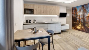 Una cocina moderna con microondas, hervidor y lavabo, un comedor con mesa y sillas, y un gran mural de un bosque en la pared.