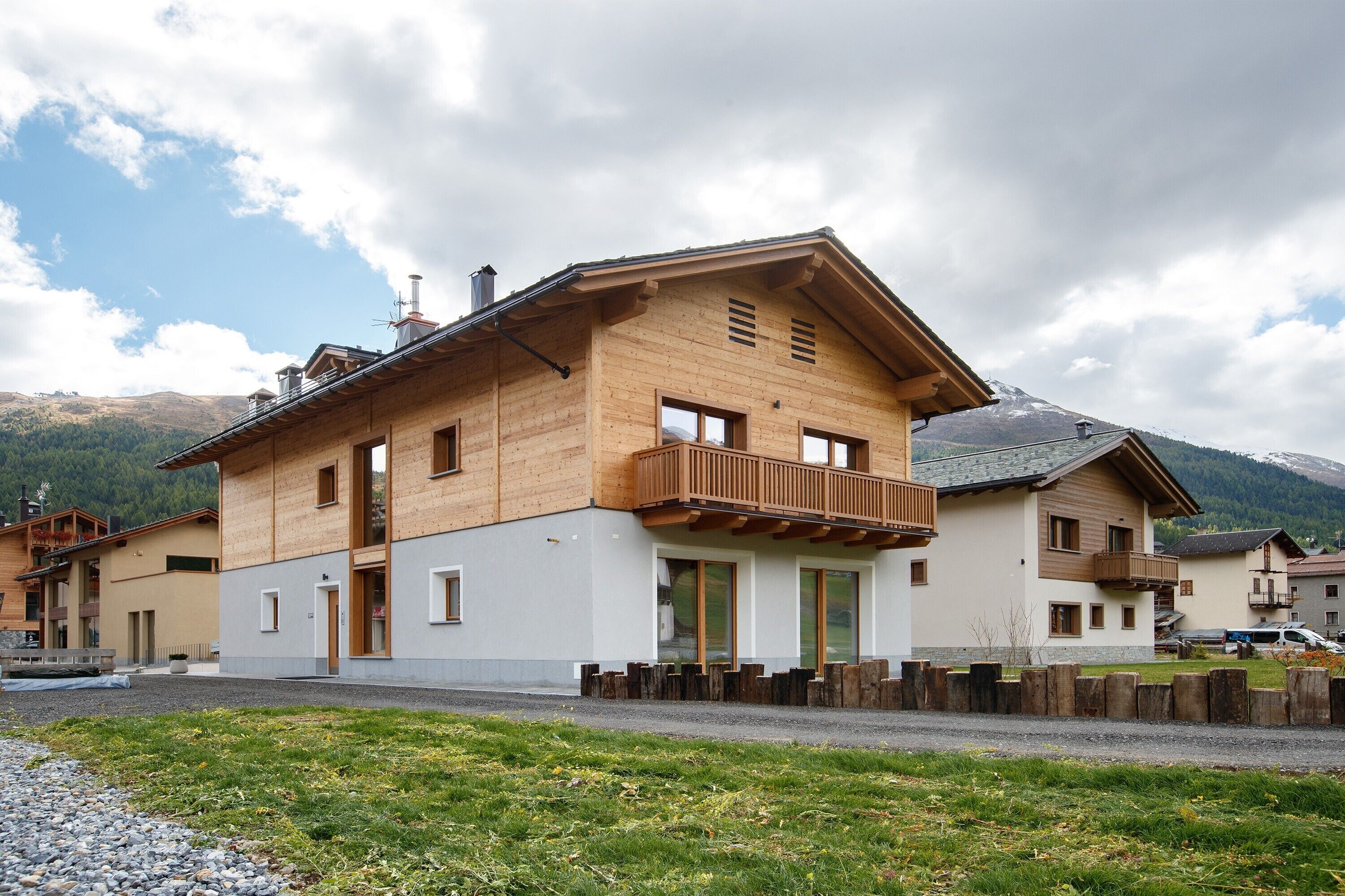 A wooden house with a balcony, a garage, and a mountain backdrop.
