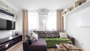 A modern living room with a sectional sofa, a flat-screen TV, a coffee table, and a potted cactus. - Park Grabiszyński Standard Studio (Wrocław)