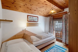 A bedroom with a wooden ceiling, a bed, a window with curtains, and a wall-mounted alphabet chart.
