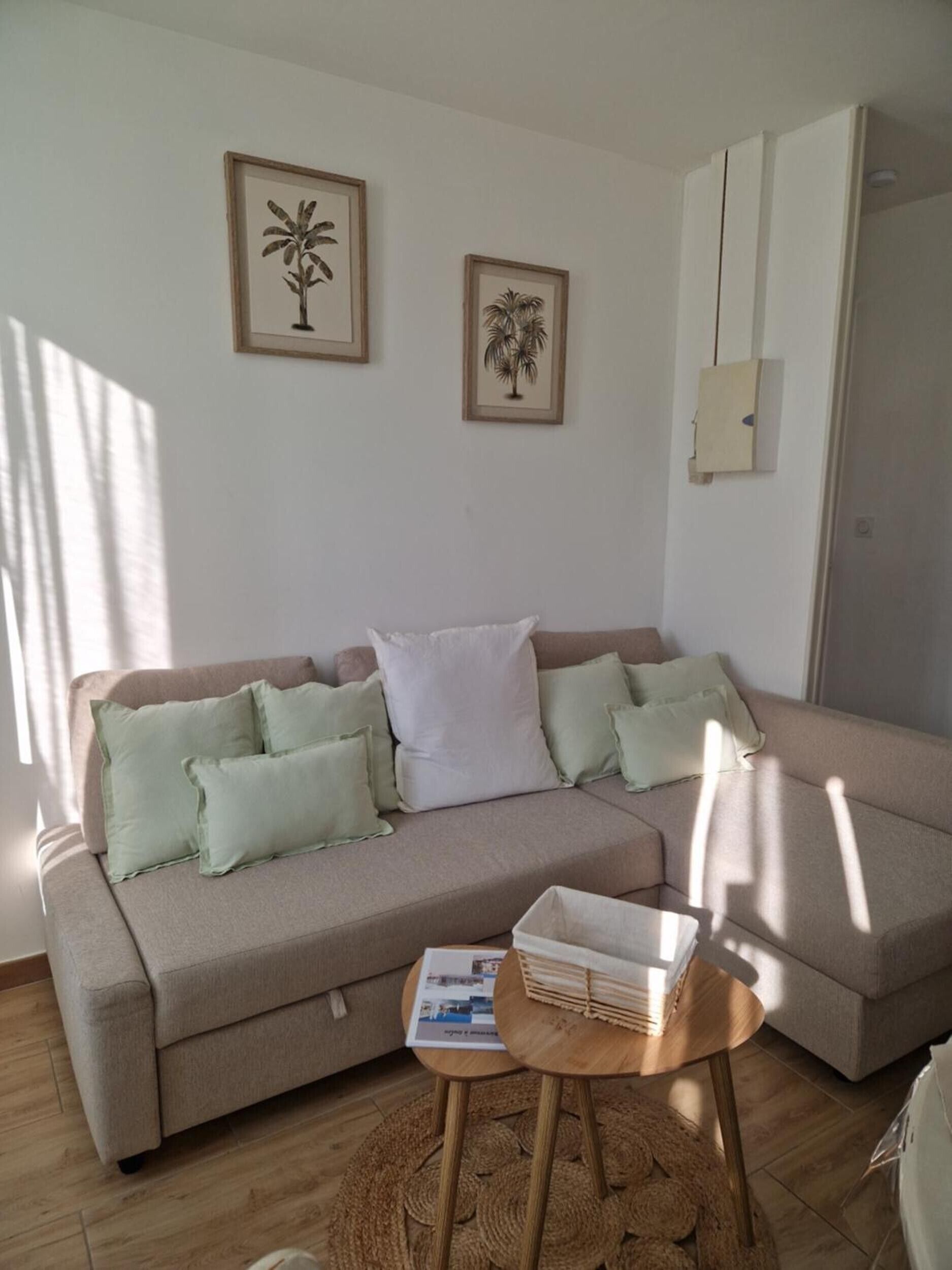 Un salón con un sofá color beige, una mesita de madera y dos cuadros en la pared.