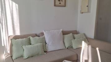 Un salón con un sofá color beige, una mesita de madera y dos cuadros en la pared.