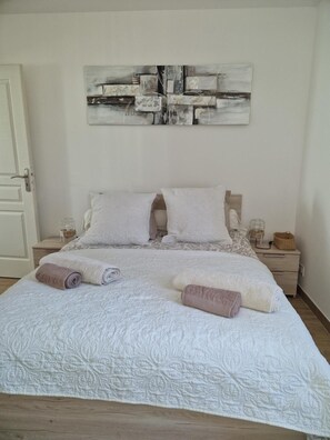 A neatly made bed with rolled towels, a wooden headboard, and a wall-mounted abstract painting. - Apartment 'Toulon, Soleil Et Douceur I' with Mountain View, Wi-Fi and Air Conditioning (Toulon)