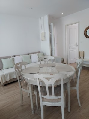 Un comedor con una mesa redonda y sillas, un sofá, una puerta y un espejo fijado a la pared.