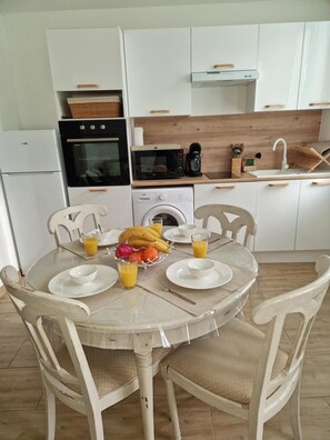 Una cocina con gabinetes blancos, microondas, cafetera y pileta.
