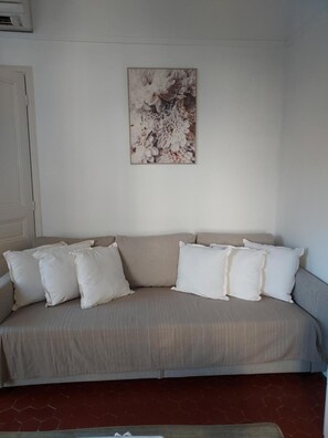 Un divano color beige con cuscini bianchi, un'opera d'arte floreale al muro e un pavimento con motivo esagonale.