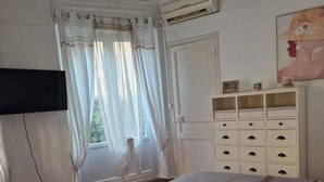 Une chambre à coucher avec un lit, une armoire, un téléviseur et une fenêtre avec des rideaux.