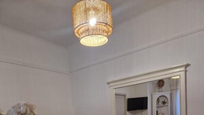 Un coin repas avec une table ronde, deux sets de table en fibres naturelles, des chaises blanches, un canapé beige, un grand miroir et un luminaire suspendu.