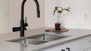 Cozinha moderna com pia de aço inoxidável, torneira preta e armários brancos.