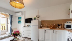 A modern kitchen with white cabinets, a wooden countertop, a washing machine, and a television. - Studio 'Soleil Et Douceur Il' with Private Garden, Wi-Fi and Air Conditioning (Sanary-sur-Mer)