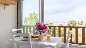 A balcony with a table set for two, a bouquet of flowers, and two glasses of orange juice. - Studio 'Soleil Et Douceur Il' with Private Garden, Wi-Fi and Air Conditioning (Sanary-sur-Mer)