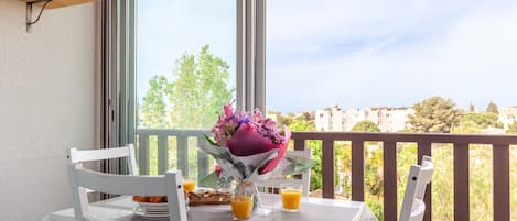 A balcony with a table set for two, a bouquet of flowers, and two glasses of orange juice.