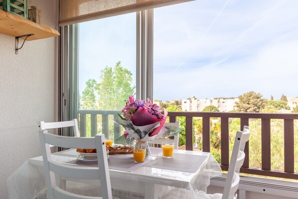 Un balcón con una mesa lista para dos personas, un ramo de flores y dos vasos de jugo de naranja.