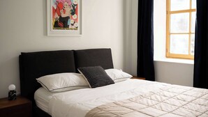 A neatly made bed with a white quilt, two pillows, and a framed poster on the wall.