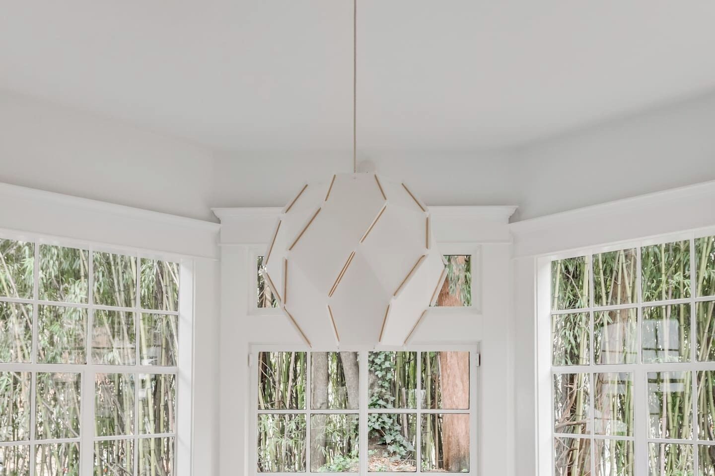 A room with large windows, a geometric light fixture, and a view of bamboo outside.