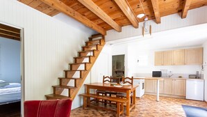 A wooden staircase leading to a bedroom, a dining area with a wooden table and chairs, and a kitchen with wooden cabinets.