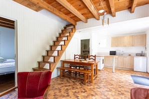 A wooden staircase leading to a bedroom, a dining area with a wooden table and chairs, and a kitchen with wooden cabinets.