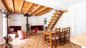 A room with a wooden ceiling, a staircase, a dining table with chairs, a sofa, and a patterned floor.