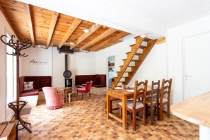 A room with a wooden ceiling, a staircase, a dining table with chairs, a sofa, and a patterned floor.