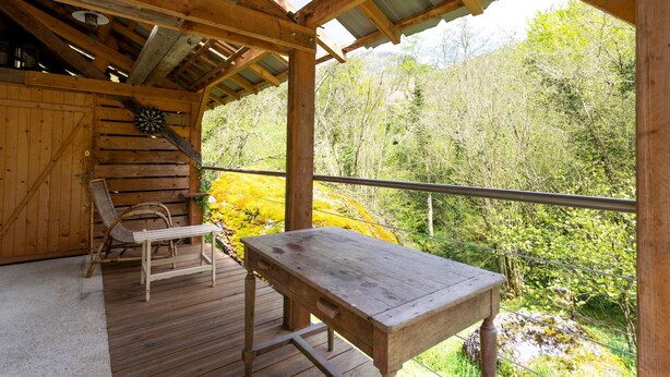A wooden deck with a table and chairs, a dartboard, and a view of a forested area.