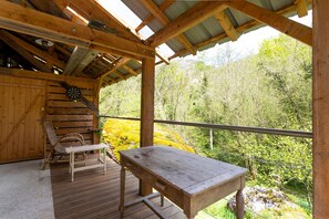 A wooden deck with a table and chairs, a dartboard, and a view of a forested area.