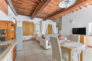 Una cucina moderna con frigorifero, fornello e pensili in legno. C'è un'area pranzo con tavolo, sedie e televisione.