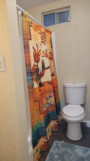 A bathroom with a colorful shower curtain, a white toilet, and a small window. - Pine Grove - Cozy Tempe 1br Apartment (Tempe)