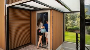 Una entrada de edificio moderna con un muro de listones de madera, una puerta de cristal y vistas a un paisaje verde a través de una ventana.