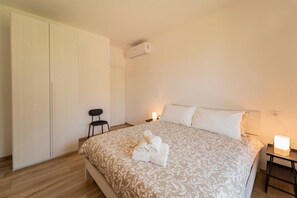 A bedroom with a bed, a chair, a wardrobe, a bedside table, and an air conditioning unit. - Holiday Apartment "1" with Lake View, Shared Pool & Shared Garden (Carlazzo)
