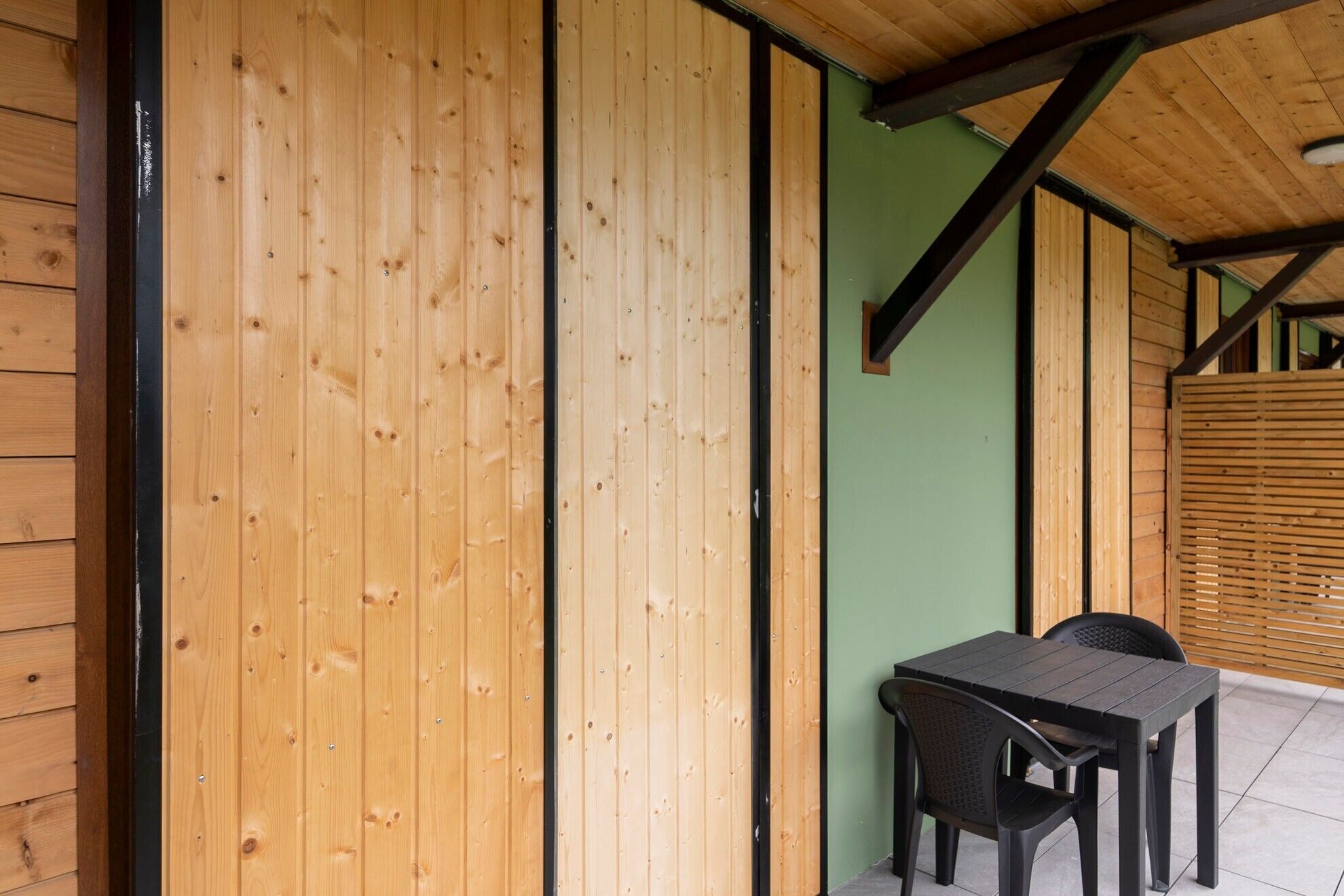 A wooden exterior wall with a black metal beam structure, a green wall, and a table with chairs.